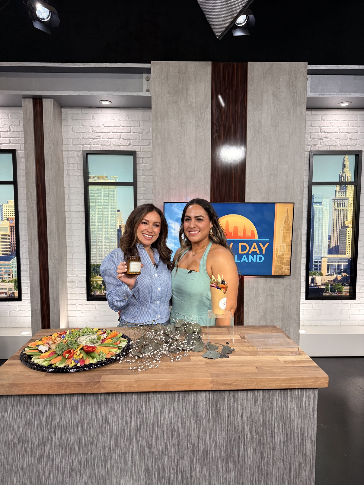 Golnar of Posh Persian Boards with a host on the New Day Cleveland studio set, with a crudité board and charcuterie cup on the table